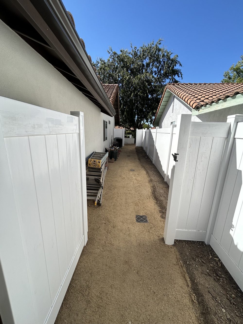 A narrow side yard between two houses, graded and finished in decomposed granite, behind a new white vinyl gate.